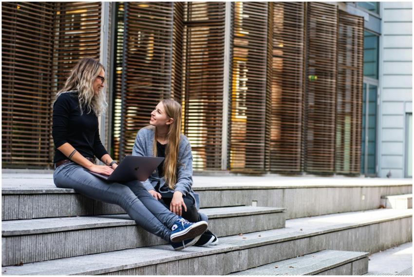 Two women sitting on steps with a laptop, discussi