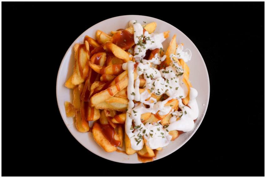 A plate of crispy fries topped with creamy sauce a