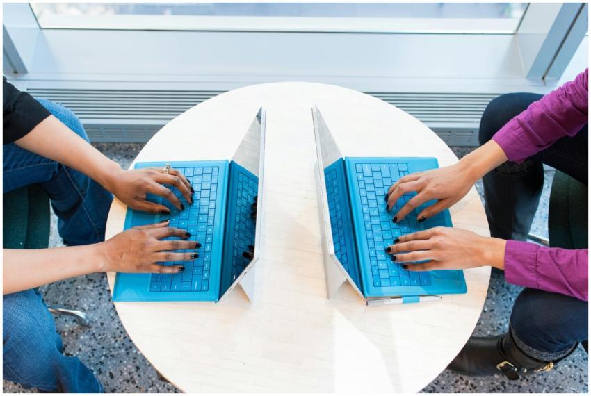 Two people working on blue laptops at a round tabl