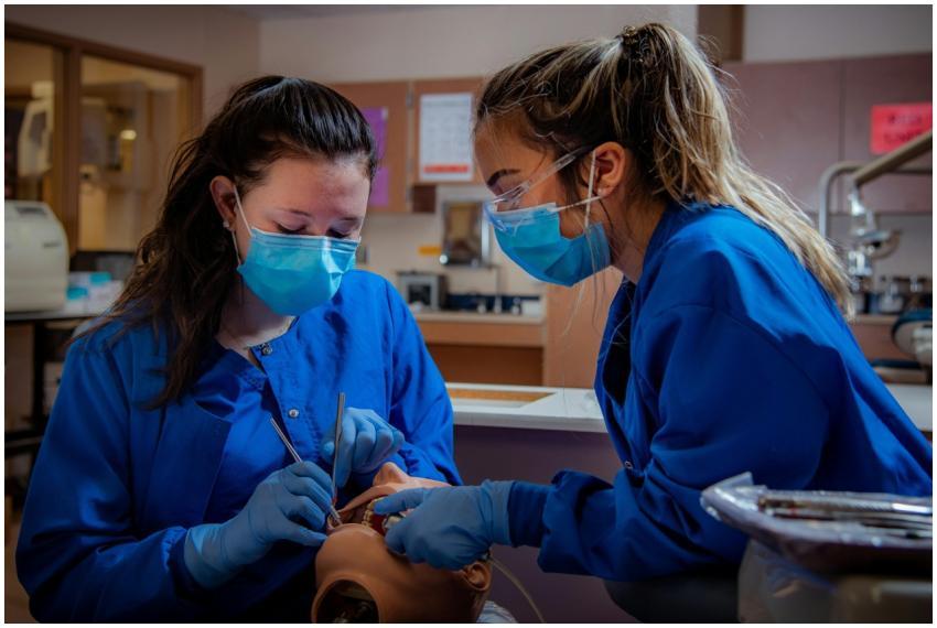 Two dental students in scrubs practice on a dummy
