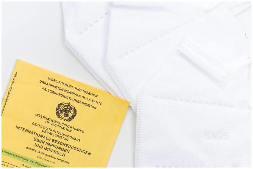 A WHO vaccination card alongside KN95 masks on a w