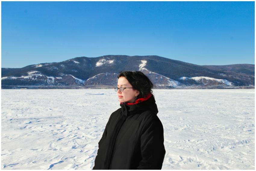 A woman stands on a snowy field with mountains in