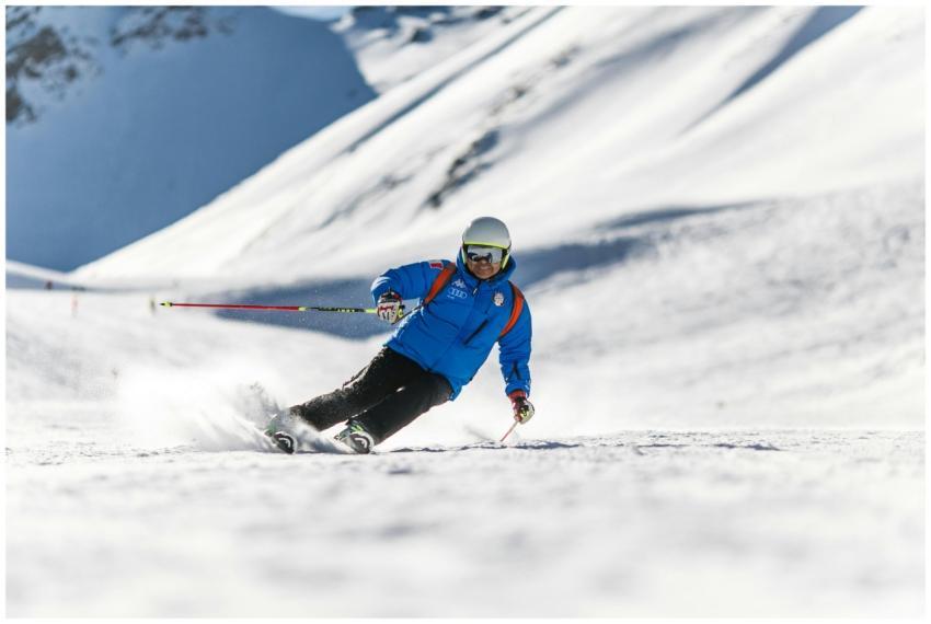 A skier carves down a sunlit snowy slope wearing p