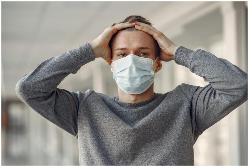 A young man wearing a medical face mask holds his