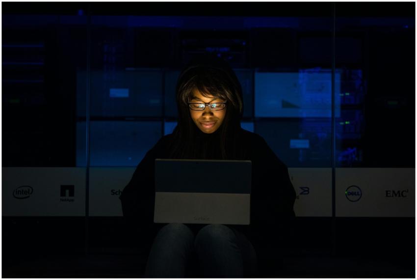 A woman uses her laptop in a dimly lit server room