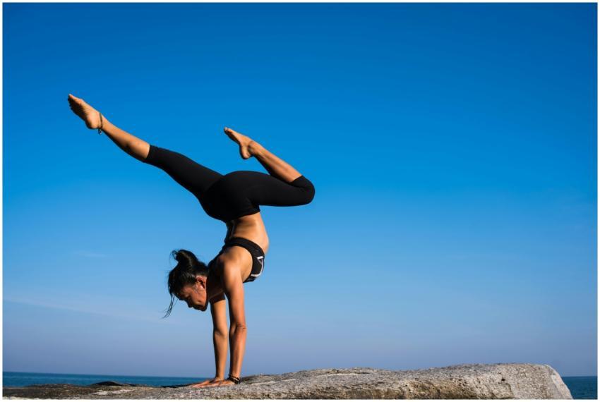 A woman performing a yoga handstand on a rock by t