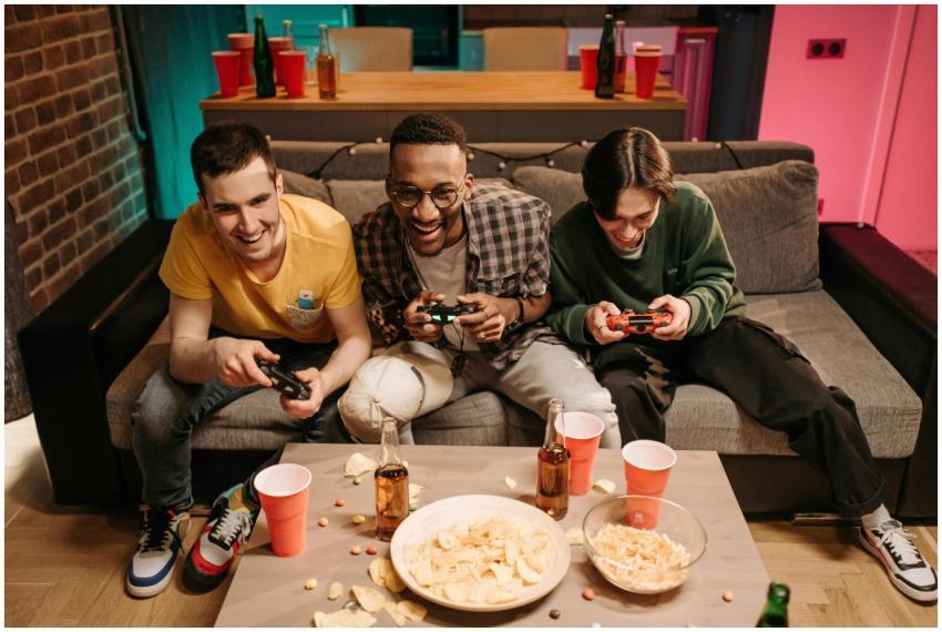 Three men playing video games together on a sofa w