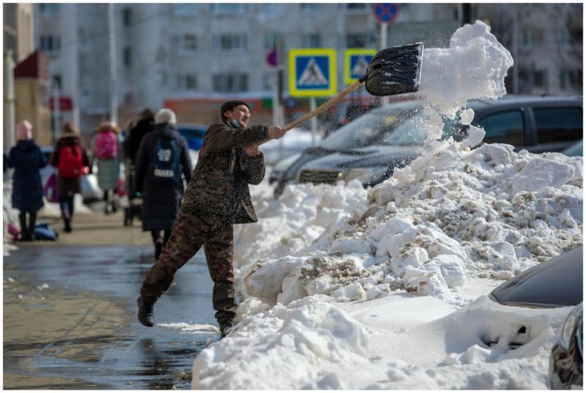 A man shoveling snow on a busy city sidewalk durin