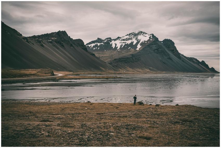 A lone traveler stands by a serene body of water u