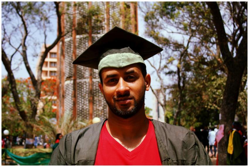 A man in a graduation cap and gown smiles confiden
