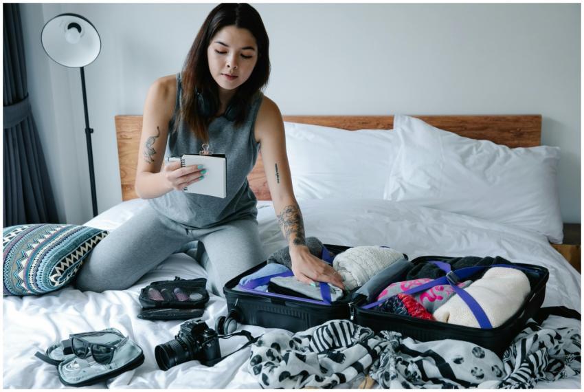 Woman sitting on bed packing a suitcase and taking