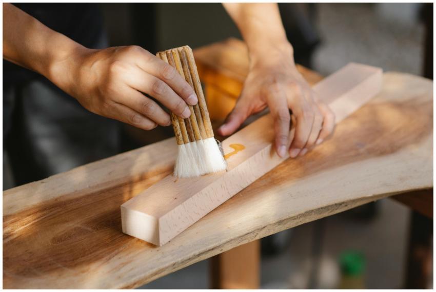 A craftsman applies oil to a wooden plank using a