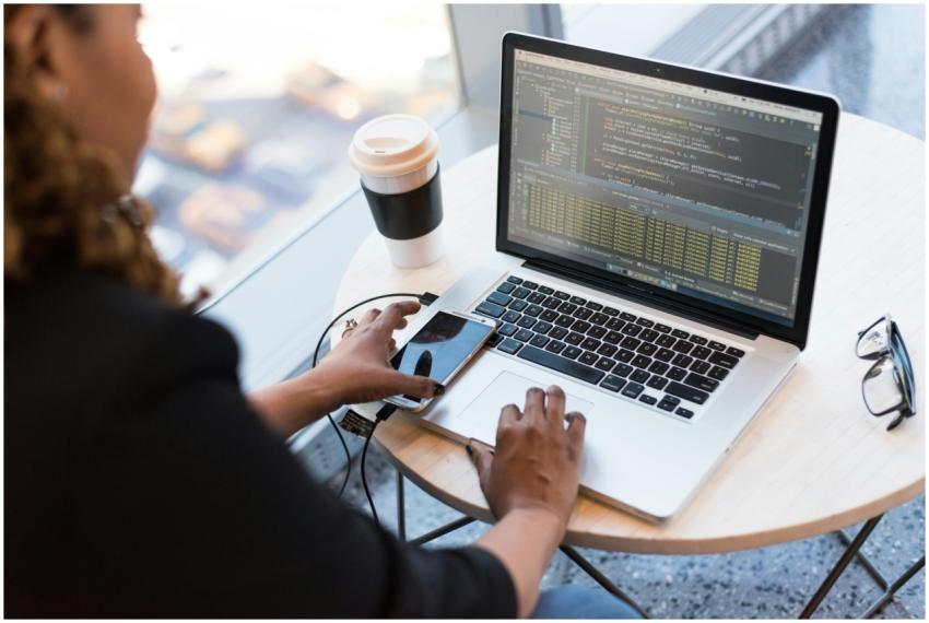 Black woman programming on a laptop with coffee, s