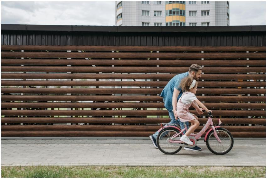A father teaches his daughter to ride a pink bicyc