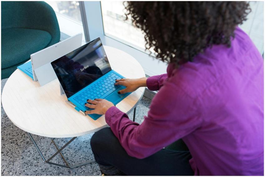A woman typing on a laptop at a round table in a m