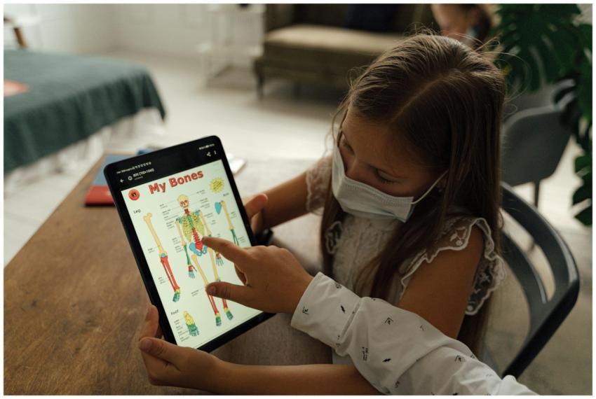A young girl wearing a face mask uses a tablet to