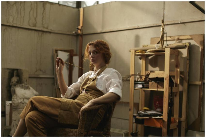 A woman artist seated in a workshop, surrounded by