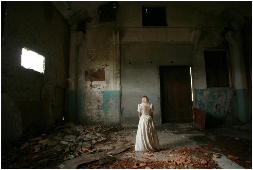 A woman in white stands in an eerie, abandoned bui