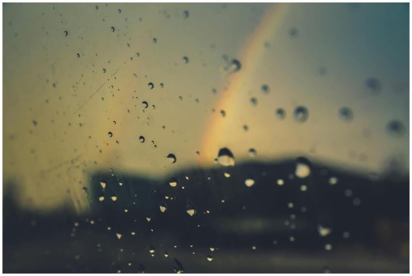 Close-up of raindrops on glass with a rainbow in t