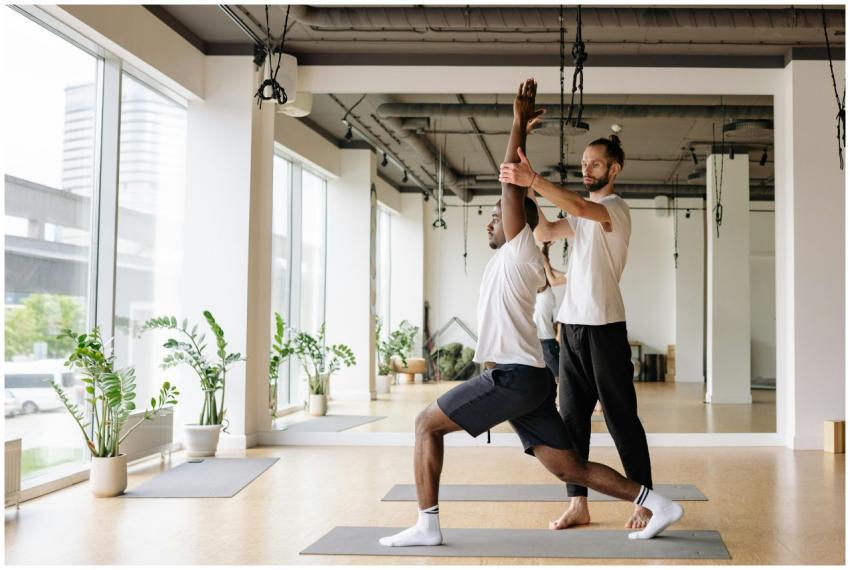 Instructor guides student in yoga pose in bright,