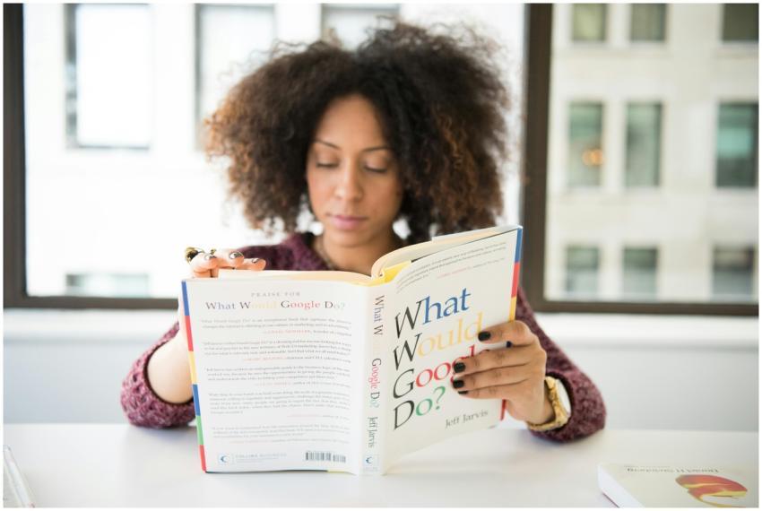 A woman reading 'What Would Google Do?' at a desk