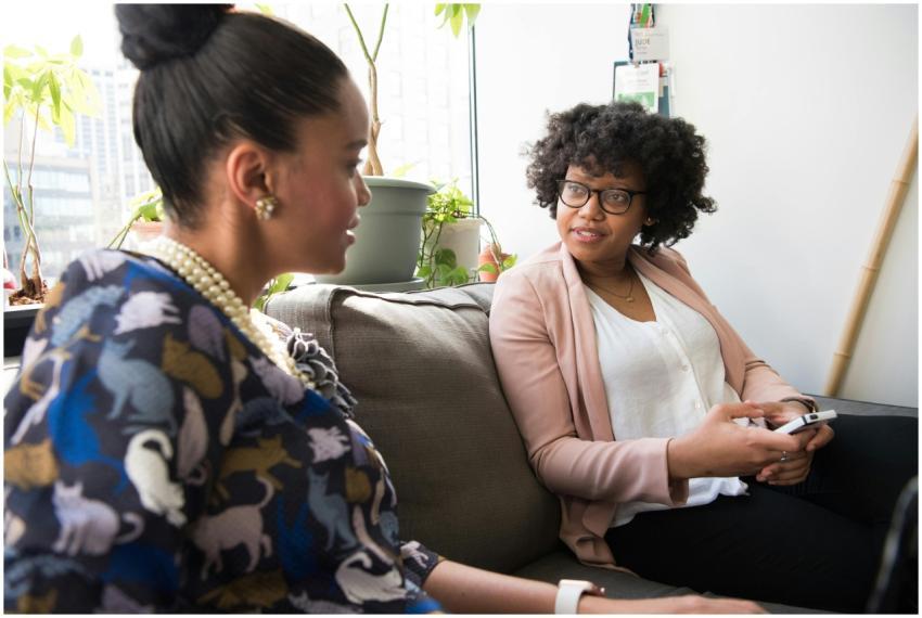 Two women sitting on sofa discussing work indoors,