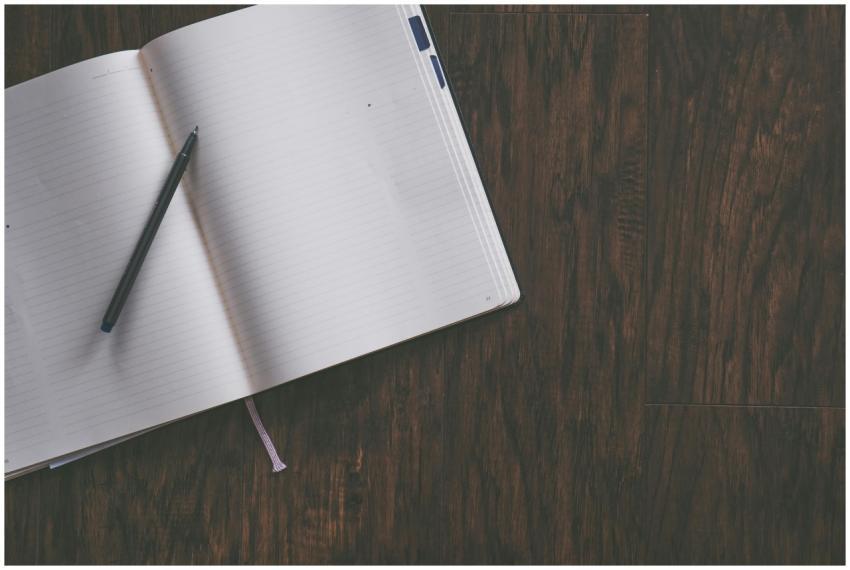 An open notebook with a pen resting on a wooden de