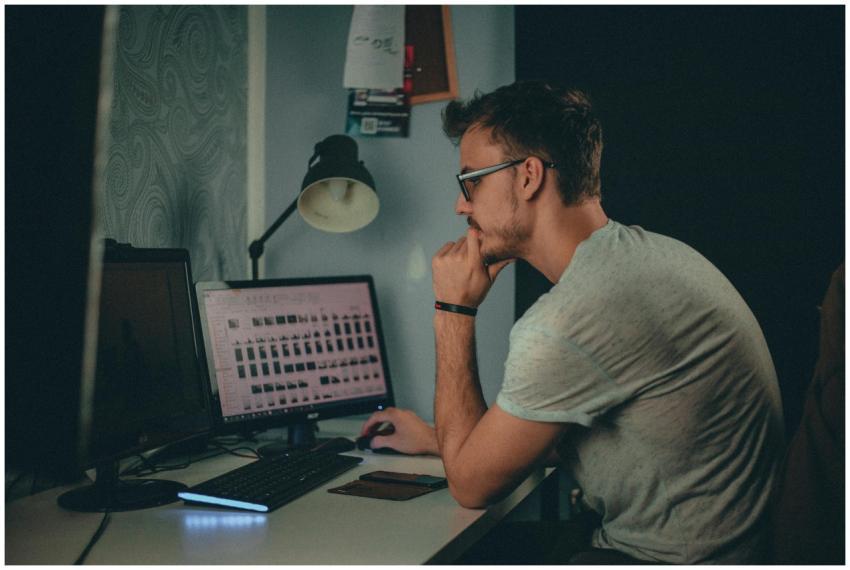Focused man using a desktop computer in a dimly li