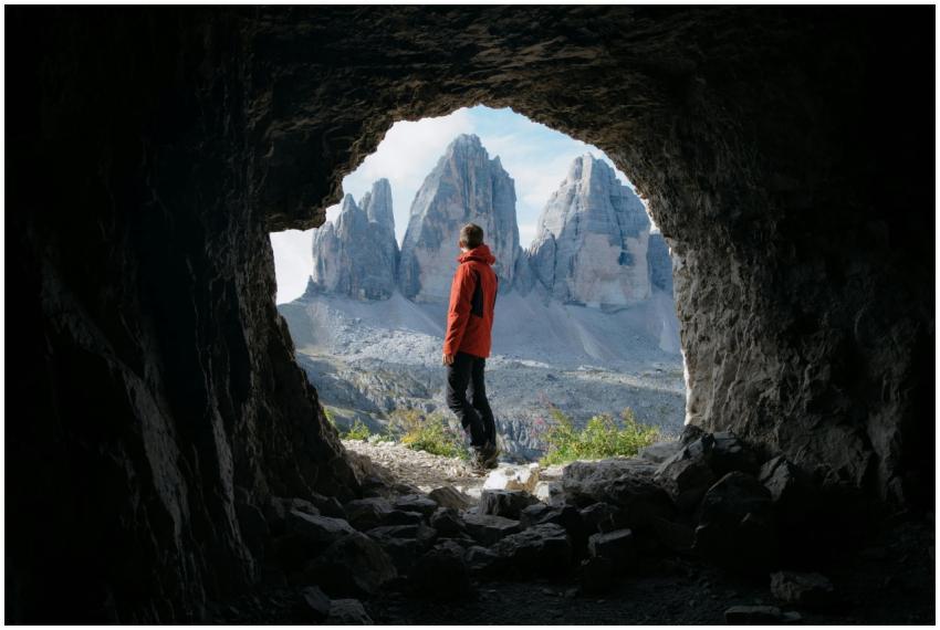 Man in red jacket standing in cave entrance, viewi