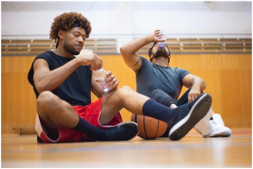 Two men sitting on indoor court, hydrating after p