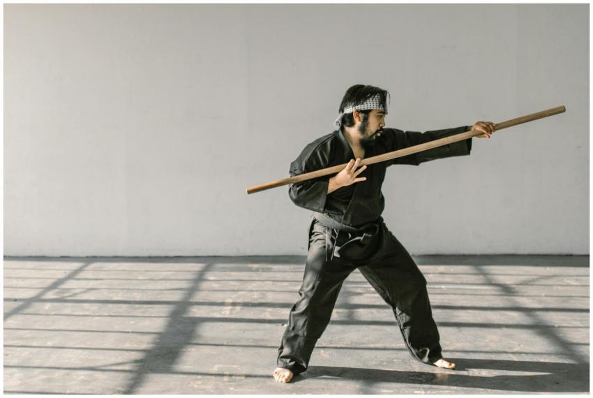 Martial artist in black gi practicing with bo staf