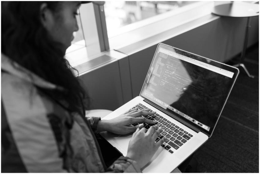 A woman typing code on a laptop in a modern indoor