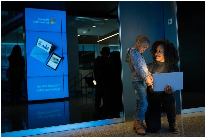 A woman and child using a laptop by a glass wall i