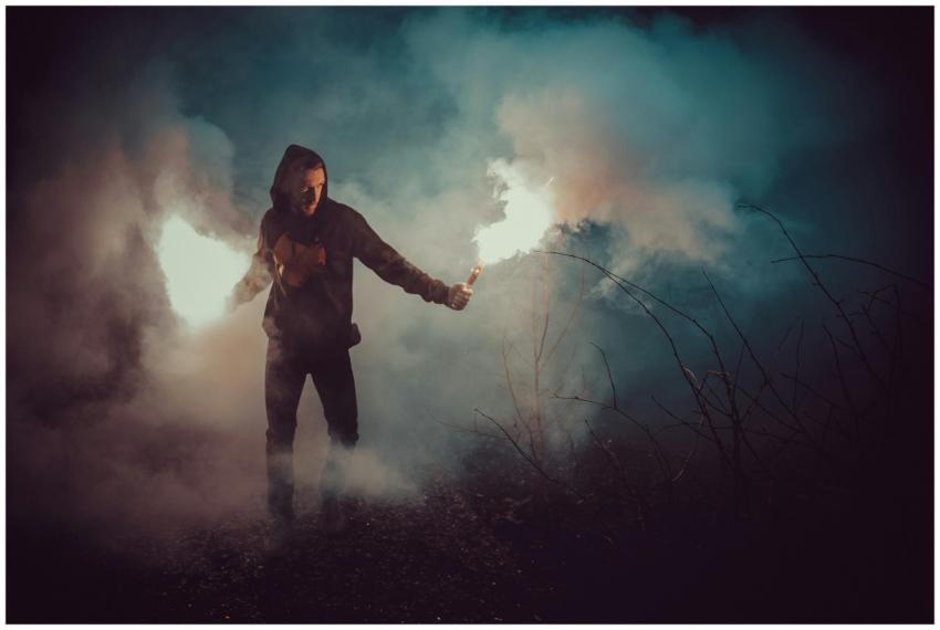 A person with a flare wanders through foggy darkne