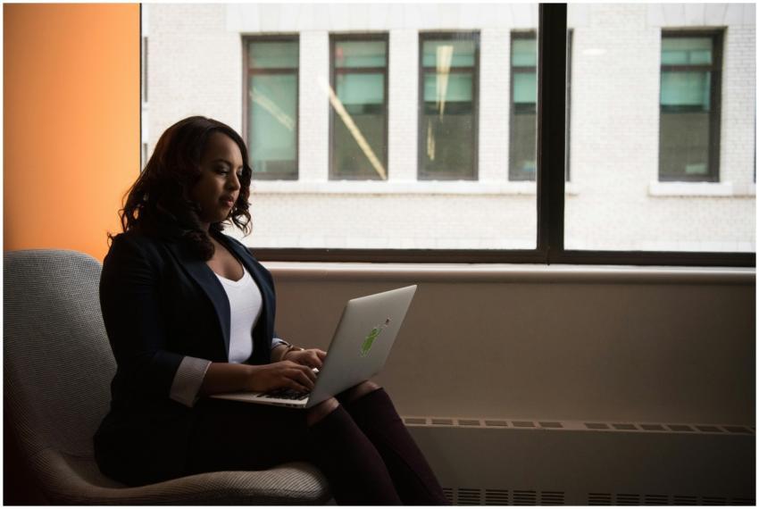 African American woman sits by window using a lapt