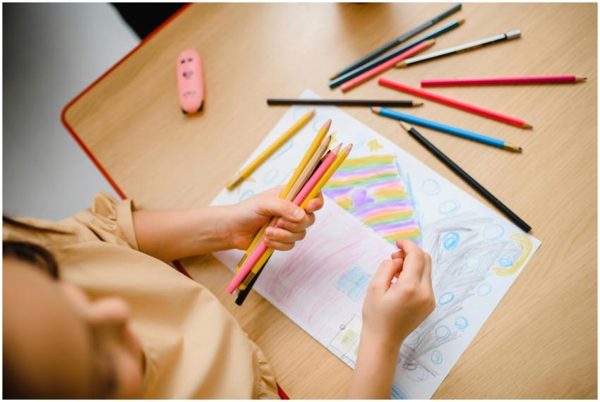 Child drawing with color pencils, expressing creat
