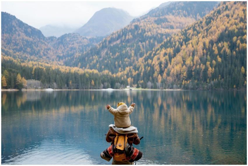 A parent and child seated on a lakeside log, enjoy