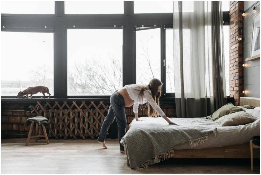 A pregnant woman arranges bed linens in a rustic b