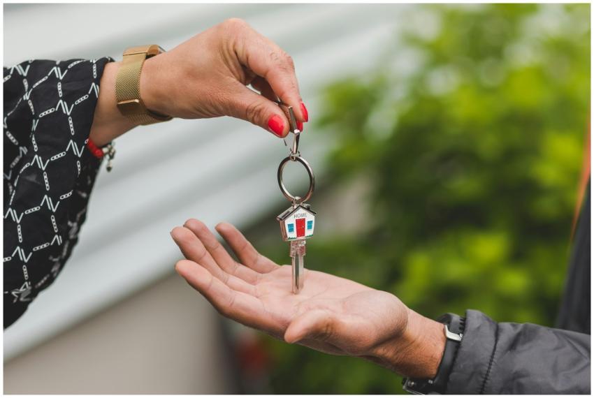Close-up of a hand handing over a key with a house