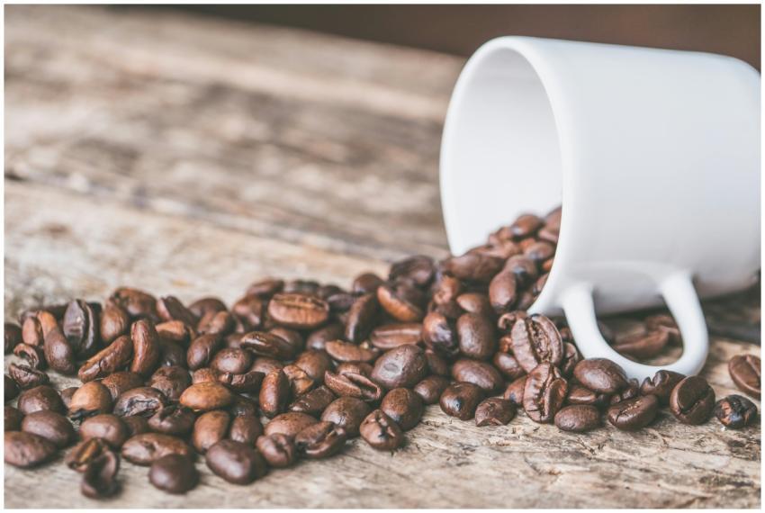 Coffee beans spilling from a white mug on a rustic