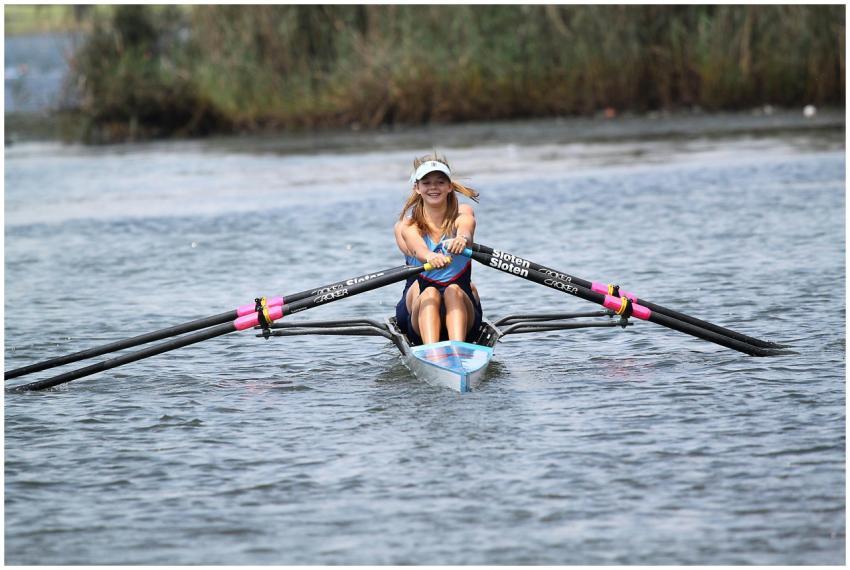 Smiling woman rowing a scull on a calm lake, enjoy