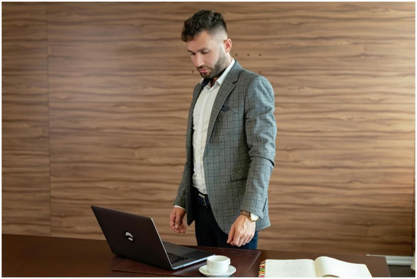 Businessman in gray blazer stands working on lapto
