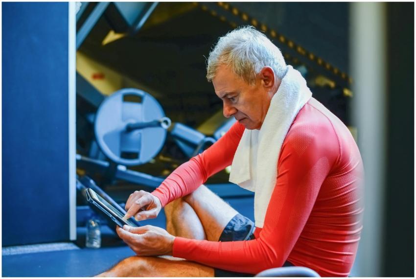 Senior man in red attire using a tablet in a gym e