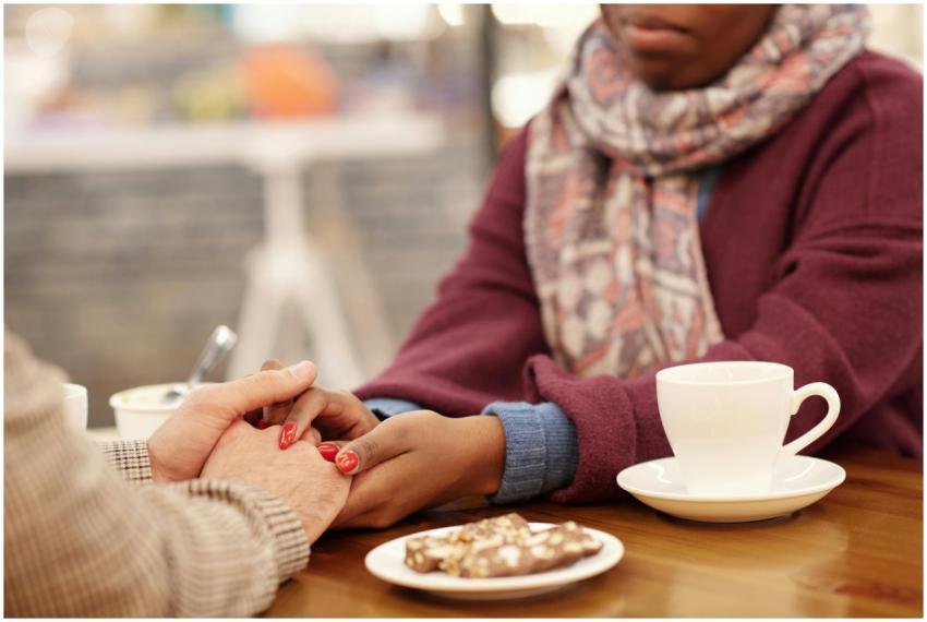 Two people holding hands at a cafe table, sharing