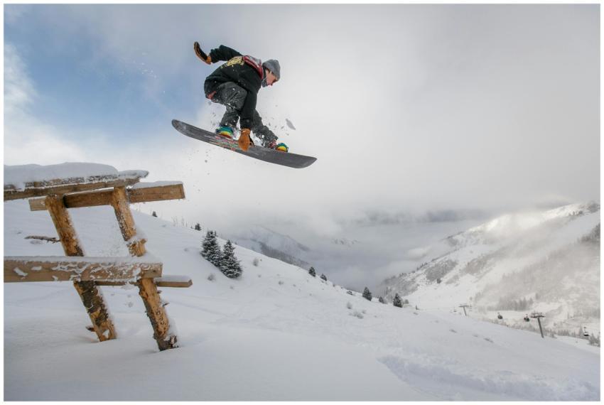 Snowboarder executing a jump over a snowy bench in