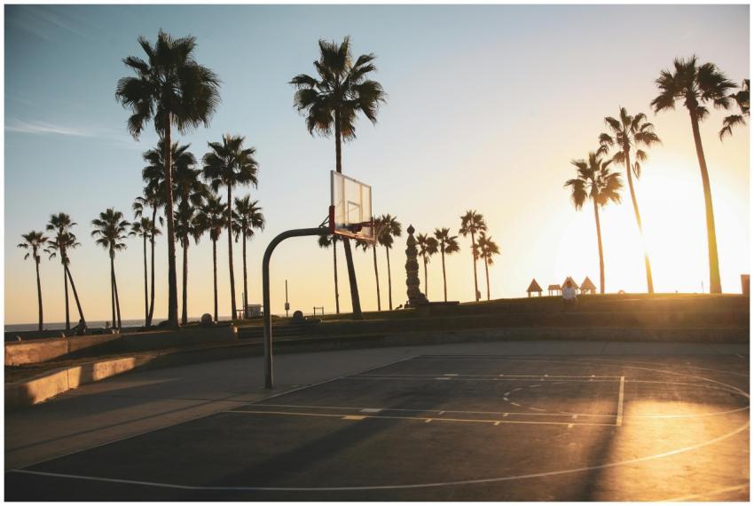 A serene sunset over a seaside basketball court wi