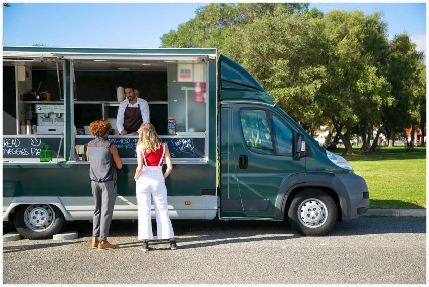 Customers ordering at a food truck parked in a sun