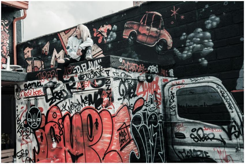 A young person seated on graffiti-covered walls de