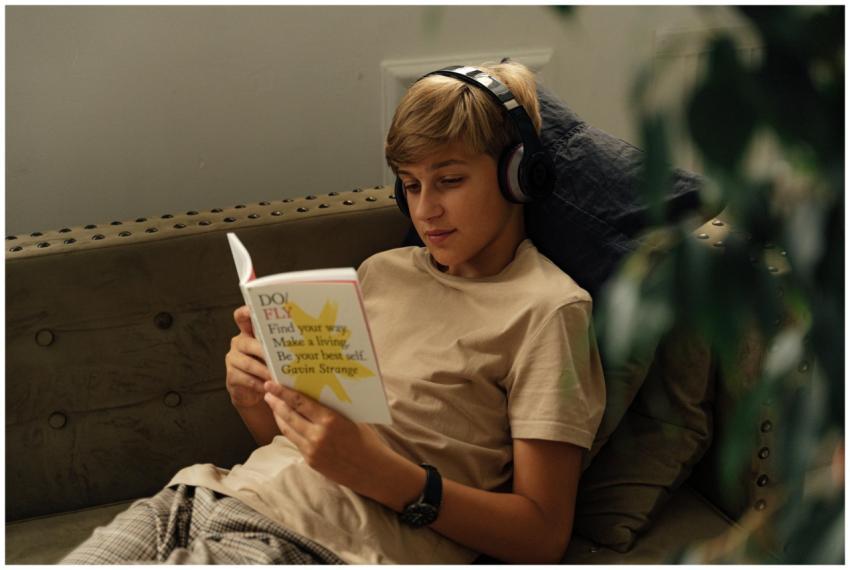 A teenager relaxes on a sofa, reading a book while