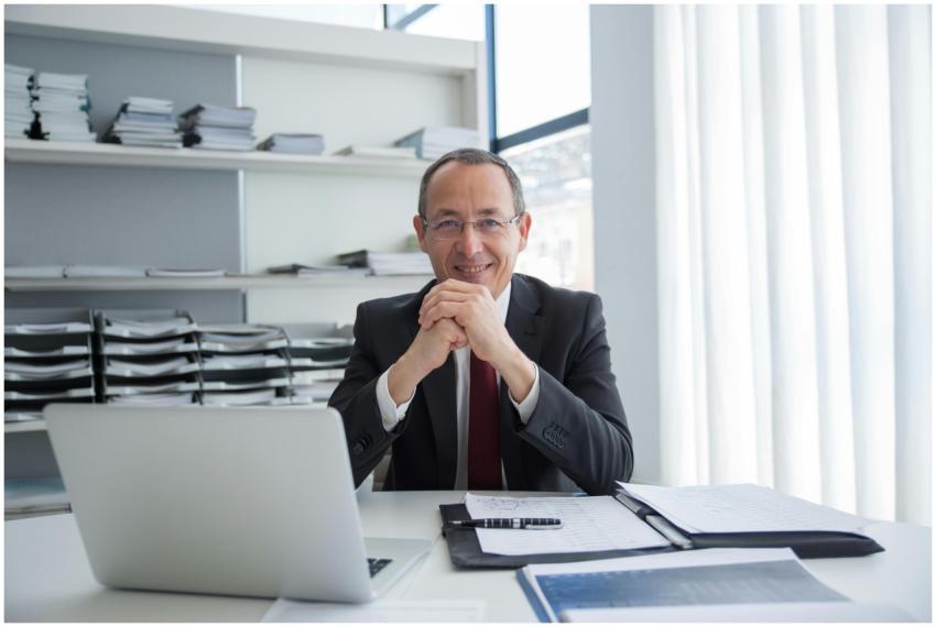 Smiling businessman in a suit with laptop and docu